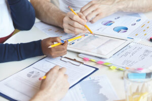 Business and finances concept. Hands of office workers holding yellow pencils, making financial report, checking statistics, drawing diagrams and charts. Man’s hand pointing at tablet with graph